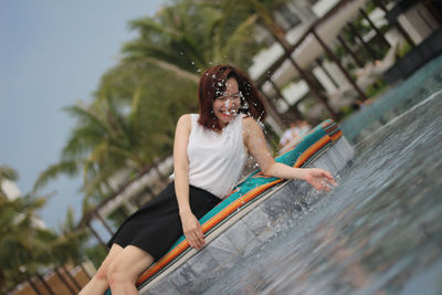 Cheerful woman splashing water while lying at poolside