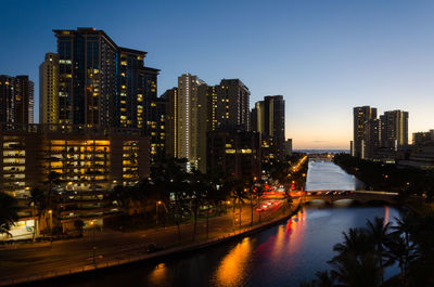 Illuminated buildings by river against sky in city at night
