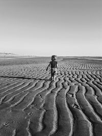 Rear view of boy walking at beach against clear sky