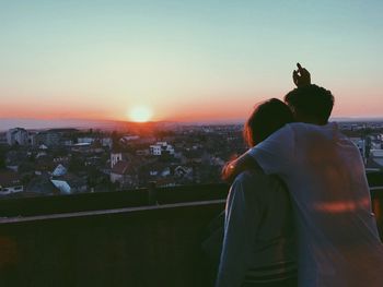 Rear view of man and woman standing against cityscape during sunset