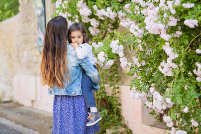 Mother and little handsome baby boy looking at bush with white roses