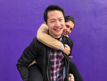 Man piggybacking girlfriend while standing against purple wall