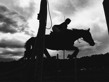 Silhouette of person on swing against cloudy sky