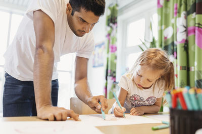 Male children assisting little girl in drawing at classroom