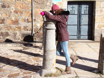 Side view of woman leaning on bollard in city