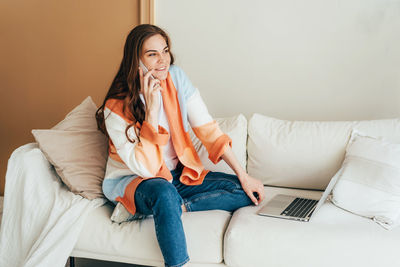 Confident business woman calling by phone while working on a laptop at home in a cozy living room 