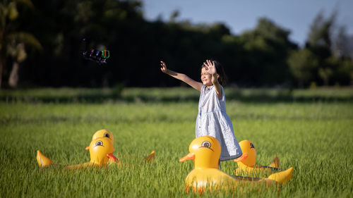 Cute girl with arms raised standing amidst toy animals on farm