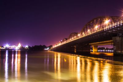 Illuminated bridge over river against sky at night