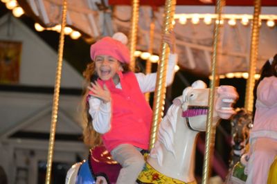 Cheerful girl enjoying while sitting on carousel horse