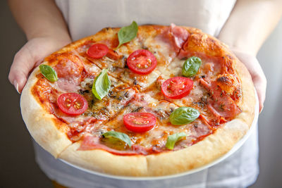 Midsection of woman holding fresh margherita pizza with salami