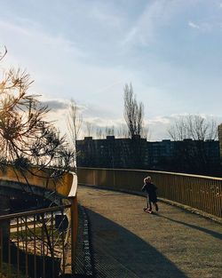 Boy standing by bare tree against sky