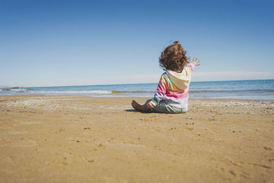 Rear view of woman sitting at beach against sky