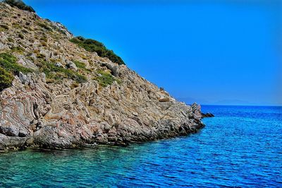 Rock formations in sea against clear blue sky