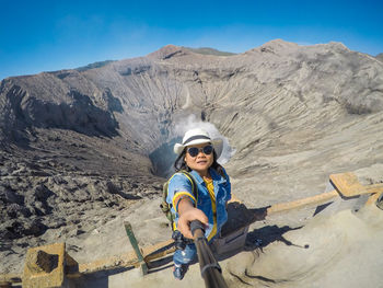 Woman wearing sunglasses standing on mountain against sky