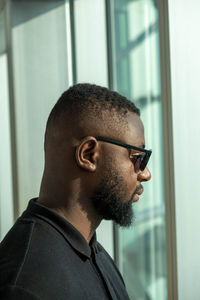 Side view of man looking through window at home