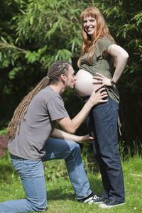 Young man kissing his pregnant wife belly on field
