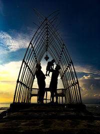Silhouette men standing by sea against sky during sunset