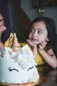 Cute girl looking at sister while sitting with birthday cake on table
