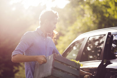 Man opening car door while holding wooden crate on sunny day