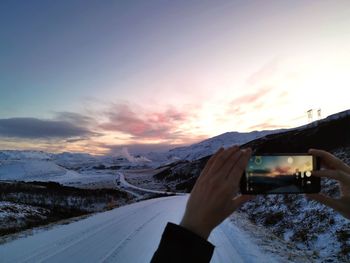 Man photographing on snow covered mountain against sky during sunset