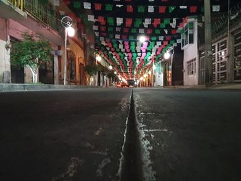 Empty road amidst illuminated buildings at night