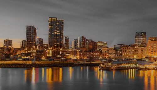 Illuminated buildings by river against sky in city