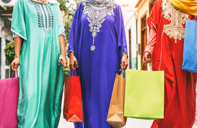 Midsection of women in traditional clothing holding shopping bags standing on street