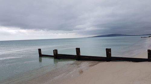 Wooden posts in sea against sky