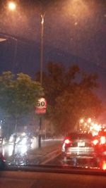 Cars on illuminated street seen through wet glass