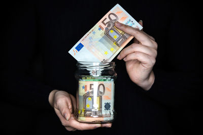 Close-up of hand holding paper against black background
