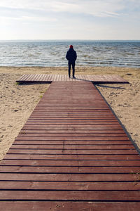  man in a black jacket stands on a wooden platform by the lake