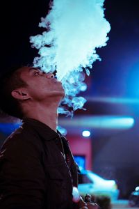 Young man smoking while standing in city at night