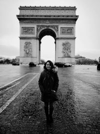 Portrait of young woman standing against triumphal arch in city
