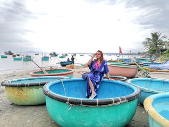 Portrait of woman wearing sunglasses sitting in boat on beach against sky