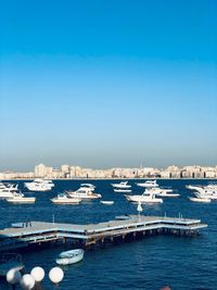 Sailboats in sea by city against clear blue sky