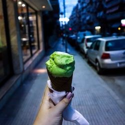 Cropped hand of woman holding ice cream cone on footpath in city
