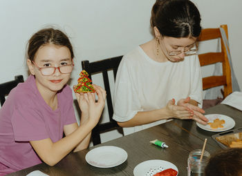 Two girls color cookies while sitting at the table.