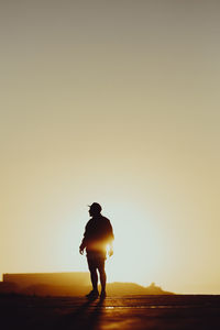 Silhouette man standing on street against sky during sunset