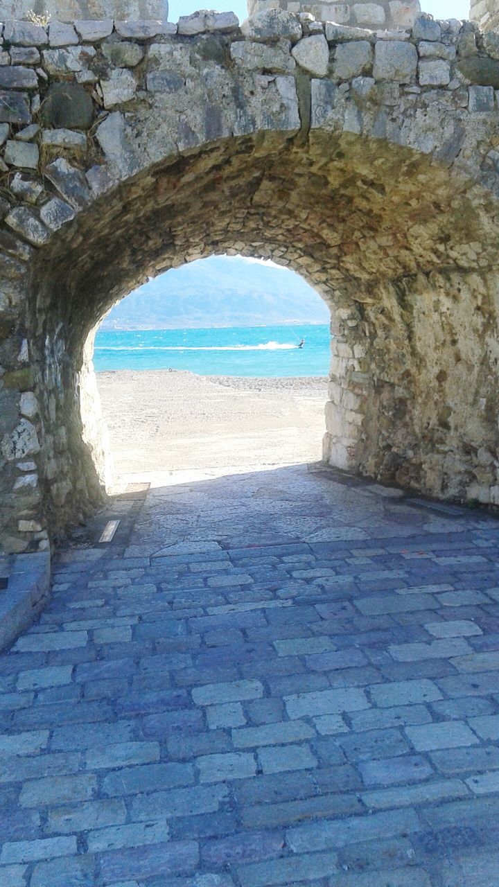 arch, built structure, architecture, water, stone wall, sky, day, sea, cobblestone, archway, sunlight, the way forward, beach, wall, tranquility, no people, nature, outdoors, wall - building feature, circle