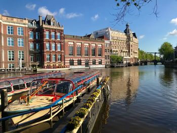 Boats moored in canal by buildings against sky in city