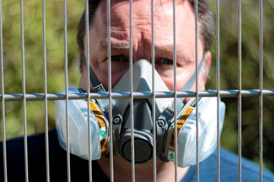 Portrait of man wearing mask seen through fence