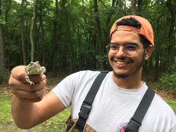 Smiling young man holding frog in forest