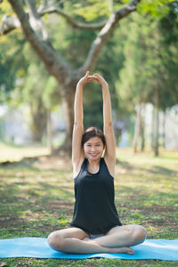 Full length of young woman with arms raised sitting at park