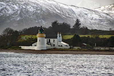 Lighthouse by lake against mountain during winter