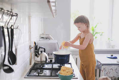 Cute toddler child in kitchen by stove helps mom cook, bright interior of kitchen