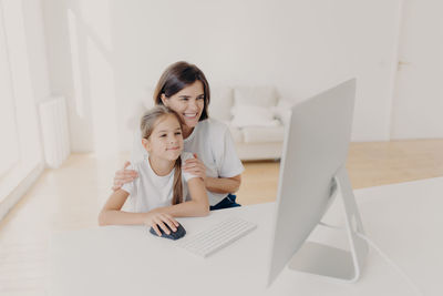 Smiling woman sitting by daughter studying on computer at home