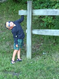Cute boy standing by railing on grassy field