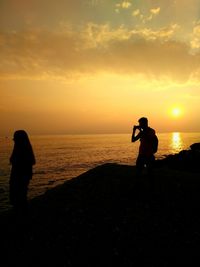 Silhouette man photographing sea against sky during sunset