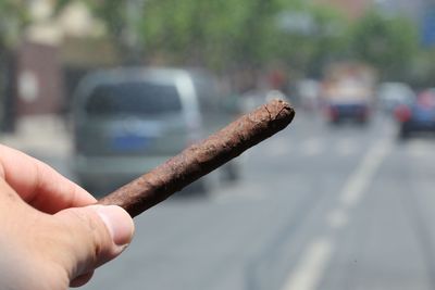 Close-up of hand holding cigarette on road