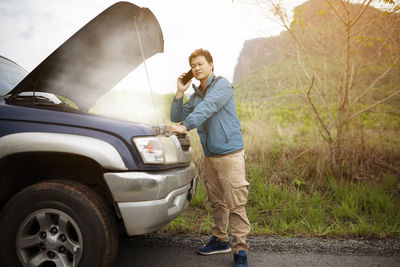 Side view of young man standing by car